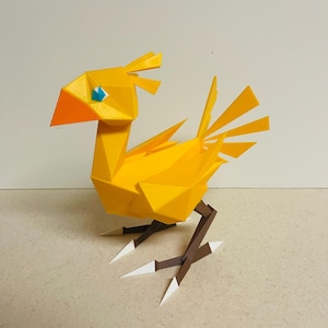 Puede incluir: Un pájaro geométrico amarillo de papel con pico naranja y ojo azul. El pájaro tiene patas marrones con puntas blancas en los pies. El diseño del pájaro es angular y estilizado, con una estética moderna.