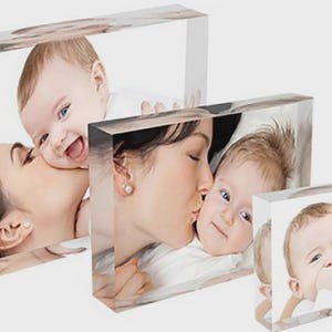 May include: Three clear acrylic photo blocks displaying images of a mother and baby. The images show the mother kissing the baby's cheek. The baby is smiling in each photo. The blocks are rectangular and vary in size.