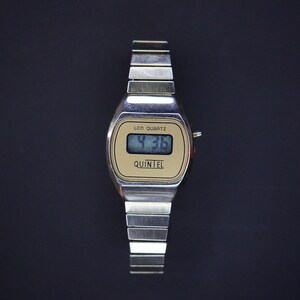 May include: A vintage silver-toned LCD Quartz watch with a rectangular face. The watch face is gold with the text "LCD QUARTZ" and "QUINTEL". The digital display shows the time as 4:36. The watch band is made of silver metal links.