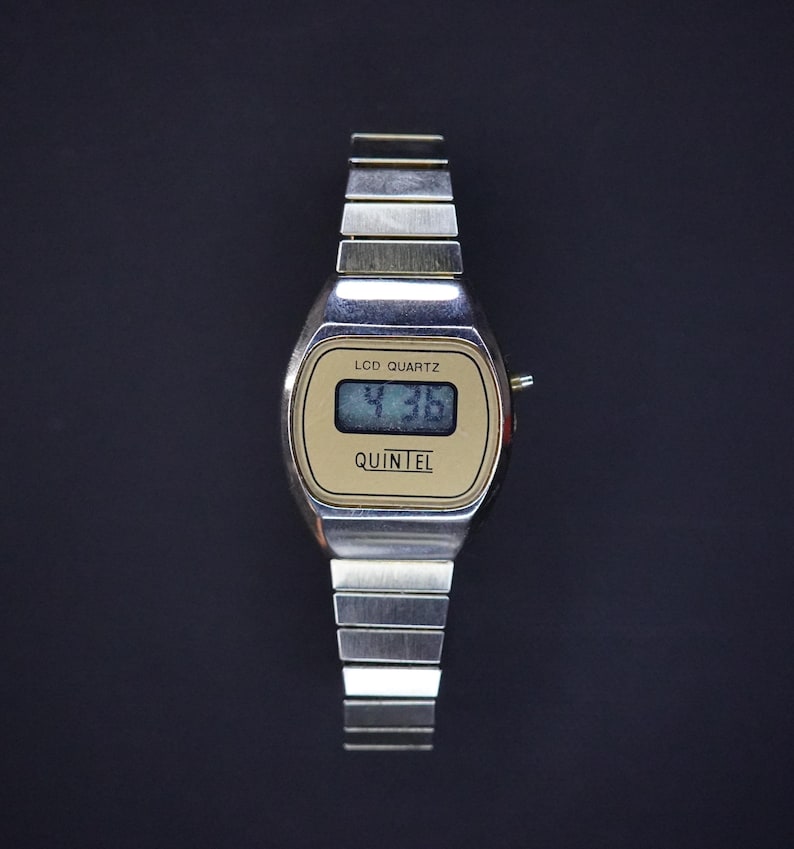 May include: A vintage silver-toned LCD Quartz watch with a rectangular face. The watch face is gold with the text "LCD QUARTZ" and "QUINTEL". The digital display shows the time as 4:36. The watch band is made of silver metal links.