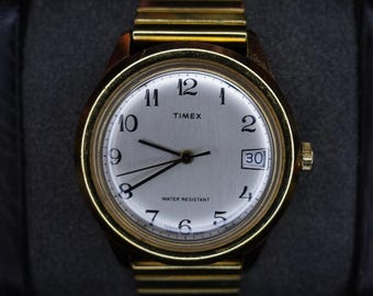 Reloj de hombre Timex Marlin vintage de 1980, de cuerda manual, con fecha, tono dorado y esfera plateada.