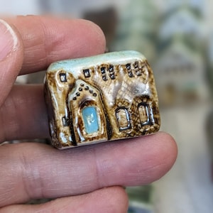 May include: A small ceramic house figurine with a brown and white glaze. The house has a blue door and windows and a white roof.