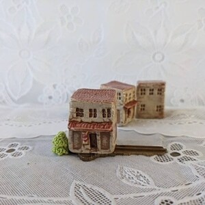 May include: Three miniature ceramic houses with red tile roofs, brown brick walls, and white windows. The houses are arranged in a row on a key.