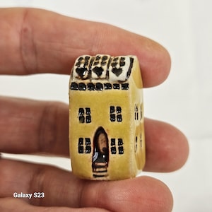 May include: A small, yellow ceramic house with black windows and a white roof. The roof has three black hearts on it.