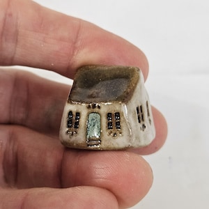 May include: A small, white ceramic house with a brown roof and black windows. The house has a green door and a small porch.