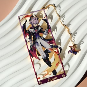 Könnte beinhalten: Rechteckiger Lesezeichen mit einer Charakterillustration mit lila Haaren, schwarzen Flügeln und einem detaillierten Outfit. Das Lesezeichen hat eine goldene Kette und einen Anhänger. Das Wort "Durin" steht unten.