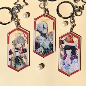 Könnte beinhalten: Drei Schlüsselanhänger aus Acryl mit Illustrationen von Charakteren im Anime-Stil. Jeder Schlüsselanhänger hat eine sechseckige Form mit rotem Rand und silbernem Ring. Die Charaktere haben detaillierte Outfits und farbenfrohes Haar. Auf hellgelbem Hintergrund.