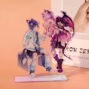 May include: Acrylic stand featuring two anime-style characters. One character has blue hair and a cat ear hat, holding an ice cream cone. The other character has purple hair and wings, also holding an ice cream cone. The stand is clear with a rectangular base.