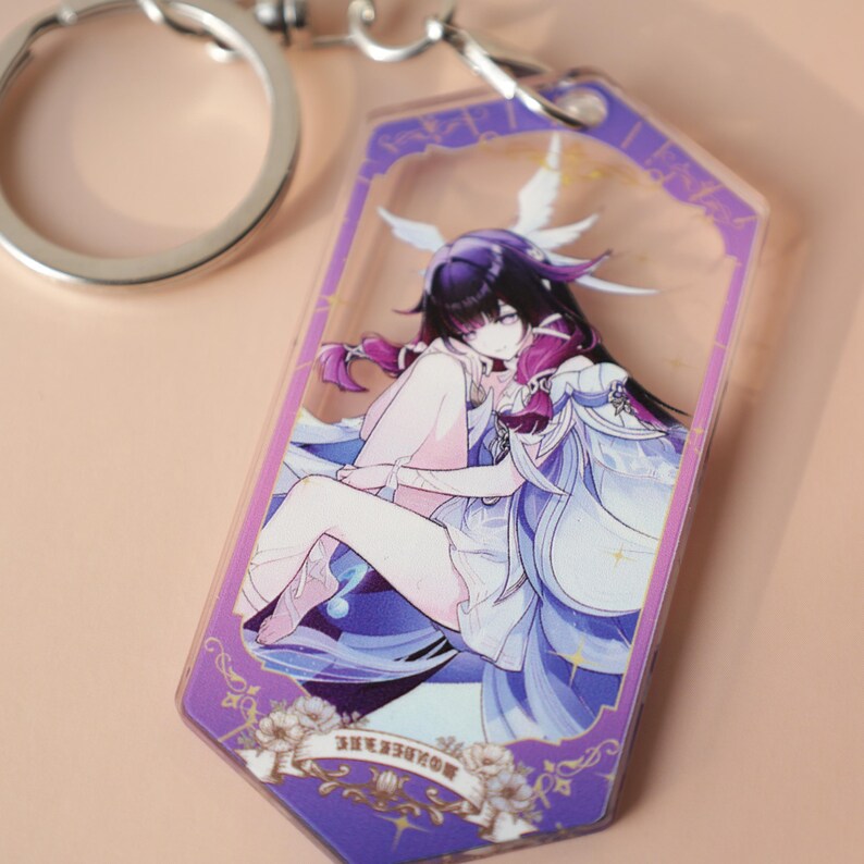 May include: A clear acrylic keychain featuring a purple-framed anime-style illustration of a character with black and purple hair, wearing a white and blue outfit. The keychain has a silver metal ring.