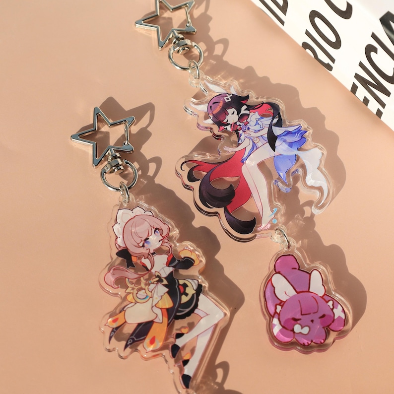 May include: Clear acrylic keychains featuring anime-style characters. One keychain has a pink-haired character in a maid outfit, another has a character in a red and blue outfit, and the last one is a pink bunny. Each keychain has a silver star-shaped clasp.