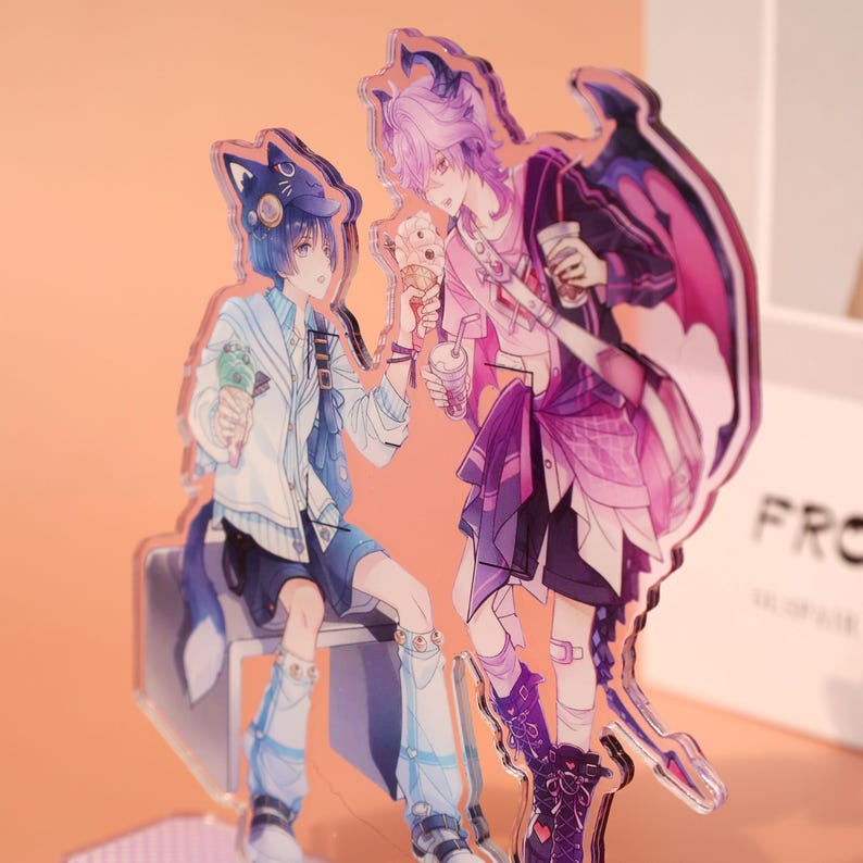May include: Acrylic stand featuring two anime-style characters. One character has blue hair and a cat-ear hat, holding ice cream. The other character has purple hair and a dragon wing design, holding a drink. The artwork has a vibrant color palette.