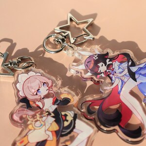 May include: Clear acrylic keychains featuring anime-style characters. The keychains have silver-colored metal clasps and star-shaped charms. The characters are depicted in various outfits with detailed facial features and colorful designs.