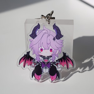 Może przedstawiać: Przezroczysty akrylowy brelok do kluczy z postacią z kreskówki z fioletowymi włosami, rogami i skrzydłami. Postać nosi czarno-fioletowy strój z różowymi akcentami. Srebrny brelok jest przymocowany u góry.