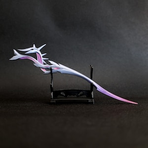 Könnte beinhalten: Ein dekorativer Haarstab mit stilisiertem Design. Der Stab hat einen silbernen Körper mit lila und rosa Akzenten. Er wird auf einem schwarzen Ständer vor dunklem Hintergrund präsentiert. Das Design umfasst spitze Elemente.