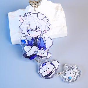 Puede incluir: Un llavero acrílico transparente con un personaje de dibujos animados con cabello blanco y ojos azules, sosteniendo una taza de café azul. El llavero también incluye dos amuletos más pequeños con forma de gato. El diseño tiene acentos azules y blancos.