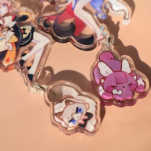 May include: A collection of clear acrylic keychains featuring colorful anime-style character designs. The keychains showcase various characters with detailed artwork, including figures with flowing hair and detailed outfits. Each keychain has a silver-colored metal loop.