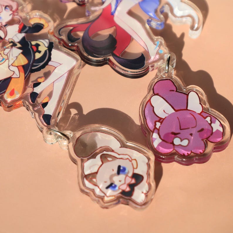 May include: A collection of clear acrylic keychains featuring colorful anime-style character designs. The keychains showcase various characters with detailed artwork, including figures with flowing hair and detailed outfits. Each keychain has a silver-colored metal loop.