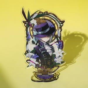 Peut inclure: Un présentoir en acrylique transparent représentant un personnage portant un chapeau et un manteau violets, encadré par une horloge et des éléments floraux. Le présentoir a une base dorée avec du texte et est posé sur un fond jaune.
