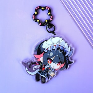 Könnte beinhalten: Ein Acryl-Schlüsselanhänger mit einer stilisierten Anime-Figur mit dunklem Haar, roten Augen und weißem Kopfschmuck in einem dunklen Outfit. Die Figur hält ein lila, hai-förmiges Accessoire. Er hat einen schwarzen, blumenförmigen Verschluss mit Punkten.