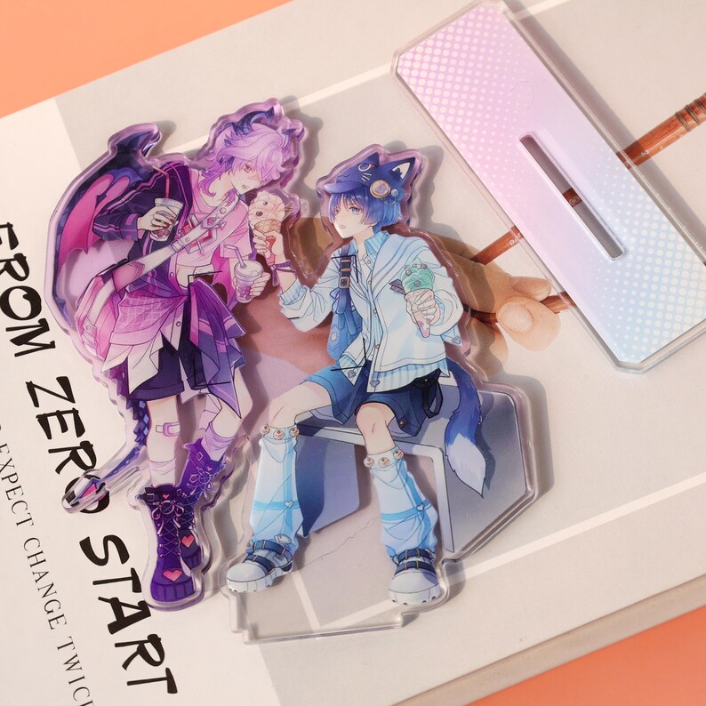 May include: Acrylic standees featuring anime-style characters with ice cream and drinks. One character has purple hair and wings, the other has blue hair and fox ears. The text "FROM ZERO START" is visible.