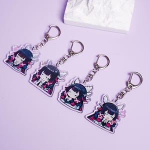 May include: Four clear acrylic keychains featuring a cartoon character with dark hair, white wings, and a pink and black outfit. Each keychain has a silver-colored keyring attached.