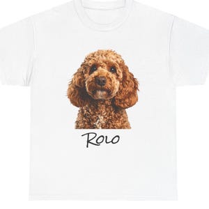 Puede incluir: Camiseta blanca con una imagen detallada de la cara de un caniche marrón. El perro tiene pelo rizado. El nombre "Rolo" está escrito en una fuente manuscrita debajo de la imagen.