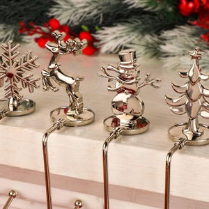Può includere: Porta calze di Natale argentati con design a fiocco di neve, renna, pupazzo di neve e albero di Natale. Ogni supporto ha una parte superiore decorativa e un gancio in metallo curvo. Decorazioni festive natalizie.