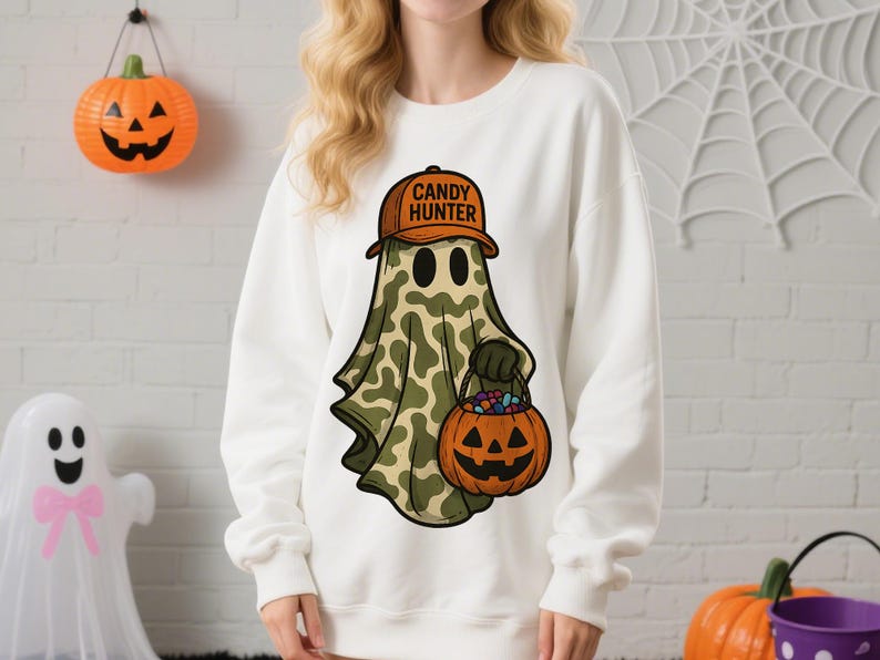 May include: White sweatshirt featuring a cartoon ghost wearing a brown hat with "CANDY HUNTER" text. The ghost has a camouflage pattern and carries a jack-o'-lantern bucket filled with candy. Halloween-themed apparel.