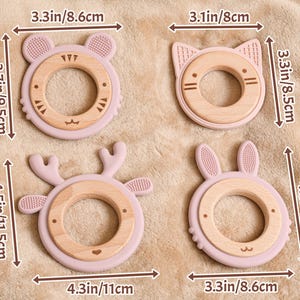 May include: Four baby teething toys in the shape of a bear, cat, deer, and bunny. Each toy has a light pink silicone exterior and a natural wood ring. The toys measure between 3.1 to 4.5 inches in length.