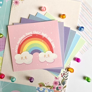 May include: A pink card with a rainbow and two clouds with faces. The text on the card reads "even rainbows have their highs and lows".