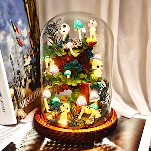 Könnte beinhalten: Ein skurriles Glaskuppel-Terrarium mit einer Miniatur-Waldszene mit leuchtenden Pilzfiguren und bunten Pilzen. Der Sockel besteht aus dunklem Holz, und die Szene wird mit sanfter Beleuchtung beleuchtet, was eine magische Darstellung erzeugt.