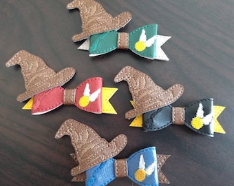 May include: Five decorative hair bows featuring a brown wizard hat and a bow with a golden snitch design. The bows are in various colors: green, red, black, blue, and brown. The background is a dark brown surface.