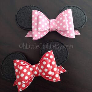 May include: Two hair accessories featuring black mouse ears with a pink polka dot bow and a red polka dot bow. The bows are centered between the ears. The text "OhLittleChild.etsy.com" is visible in the image.
