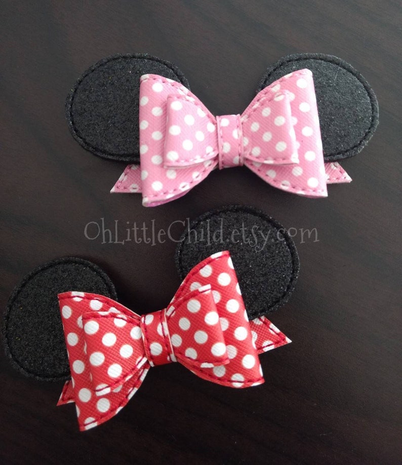 May include: Two hair accessories featuring black mouse ears with a pink polka dot bow and a red polka dot bow. The bows are centered between the ears. The text "OhLittleChild.etsy.com" is visible in the image.