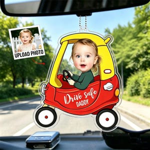 May include: A personalised car charm with a child in a red and yellow toy car design. The charm has the text "Drive safe DADDY" and includes a photo upload area. The charm hangs from a chain.