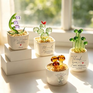May include: Four decorative glass plant sculptures in small white pots. The plants include a lily of the valley, a cactus, a cluster of green orbs, and mushrooms. Each pot has a message of thanks, making them ideal gifts for teachers.
