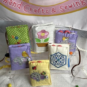 May include: A collection of small, colorful fabric pouches, each with unique embroidered designs. The pouches feature floral, bird, and sewing-themed motifs. The banner above reads "Hand Crafts & Sewing".
