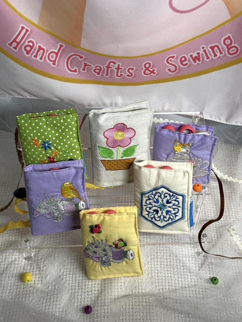 May include: A collection of small, colorful fabric pouches, each with unique embroidered designs. The pouches feature floral, bird, and sewing-themed motifs. The banner above reads "Hand Crafts & Sewing".