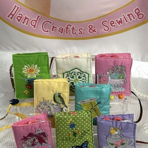 May include: A collection of colorful, embroidered sewing needle cases. Each case features a unique design, including flowers, birds, and butterflies. The cases are displayed against a backdrop with the text "Hand Crafts & Sewing".