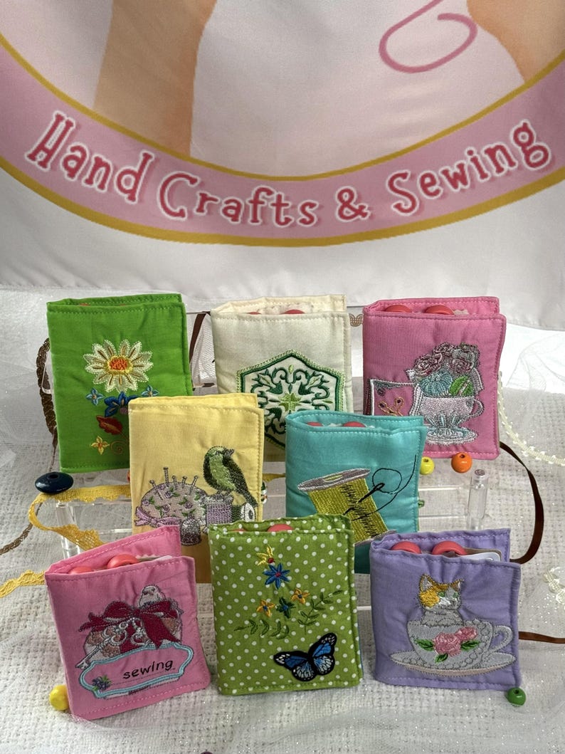 May include: A collection of colorful, embroidered sewing needle cases. Each case features a unique design, including flowers, birds, and butterflies. The cases are displayed against a backdrop with the text "Hand Crafts & Sewing".