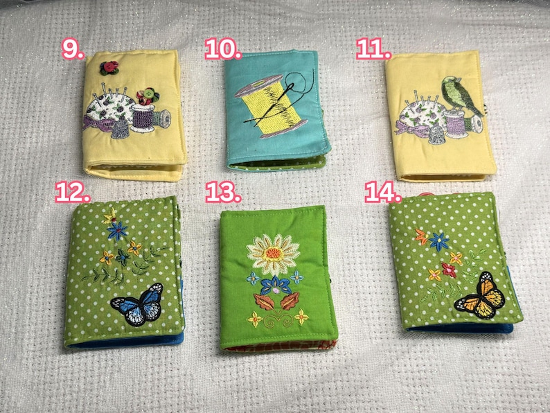May include: A collection of six small, embroidered needle cases. The cases feature various designs, including a spool of thread, a bird, butterflies, and floral patterns. The cases are in shades of yellow, teal, and green, with polka dots and detailed stitching.