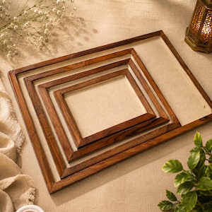 Puede incluir: Un conjunto de cuatro marcos rectangulares de madera encajados con un acabado de veta de madera marrón oscuro natural. Cada marco presenta un borde liso y plano que rodea un fondo texturizado de color beige claro.