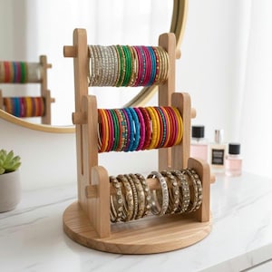 May include: A wooden bangle stand with three levels, showcasing a variety of bangles. The top level holds silver and green bangles, the middle level has a rainbow of colours, and the bottom level features gold bangles with rhinestones.