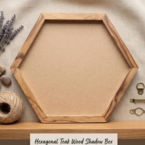 Peut inclure: Cadre hexagonal en bois de teck avec un intérieur marron clair. Le cadre est en bois naturel et a une forme géométrique. Le texte en bas indique : Hexagonal Teak Wood Shadow Box Frame - Blanks for Creativity.