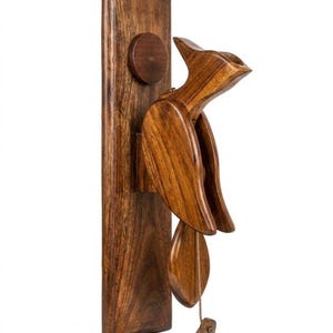May include: A wooden bird-shaped wall-mounted bottle opener. The opener is made of dark brown wood and features a bird design with a long beak and outstretched wings. The opener is attached to a rectangular wooden base.