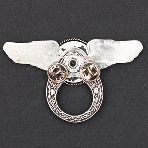 May include: Silver winged pin with a circular design and two pin backs. The wings are spread out and the circle has a detailed design.