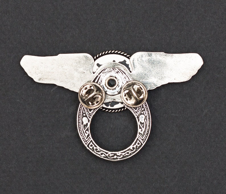 May include: Silver winged pin with a circular design and two pin backs. The wings are spread out and the circle has a detailed design.