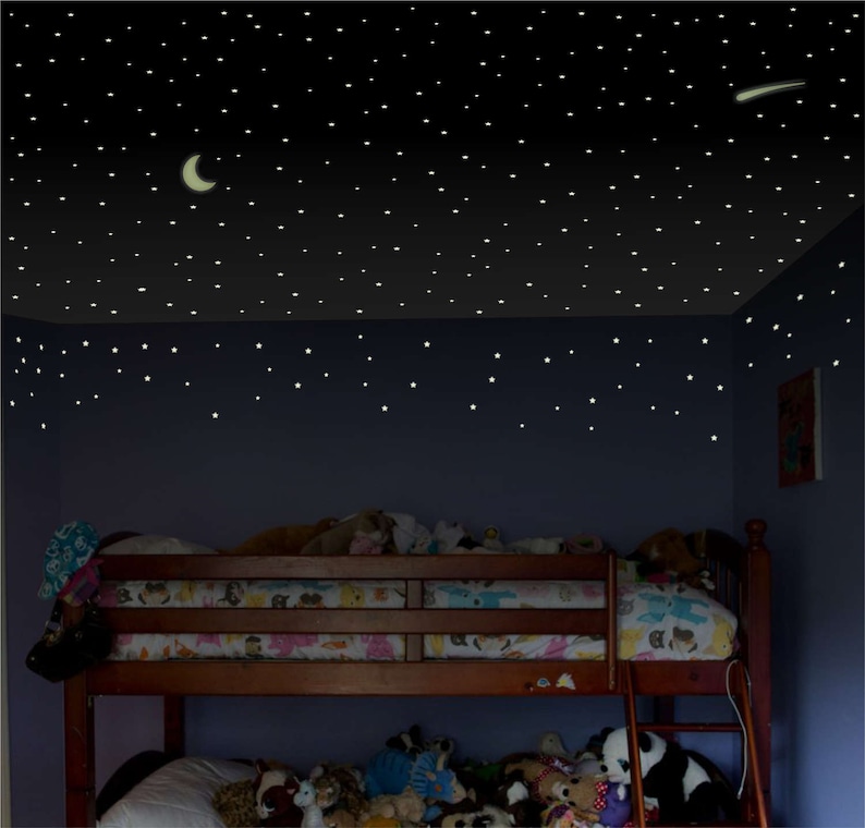 Puede incluir: Una litera de madera con un colch&oacute;n de estampado blanco y colorido y un colch&oacute;n de estampado blanco y gris en la litera inferior. La habitaci&oacute;n tiene una pared azul oscuro con estrellas que brillan en la oscuridad y una luna creciente en el techo.
