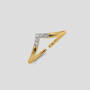 May include: A gold-colored ring with a V-shaped design. The ring features a row of small, clear gemstones set in the center of the V. The ring has an open design, with the ends of the band not connected.