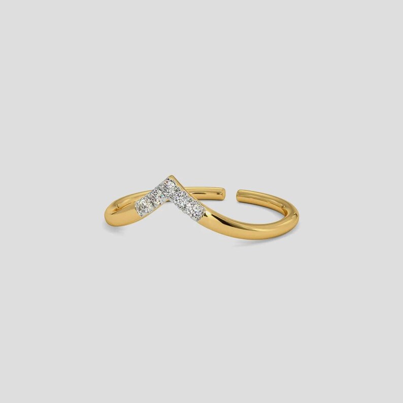 May include: A gold-colored ring with a V-shaped design. The ring features a row of small, clear gemstones set in the center of the V. The ring is open at the back, allowing for some size adjustment. The ring is set against a light gray background.